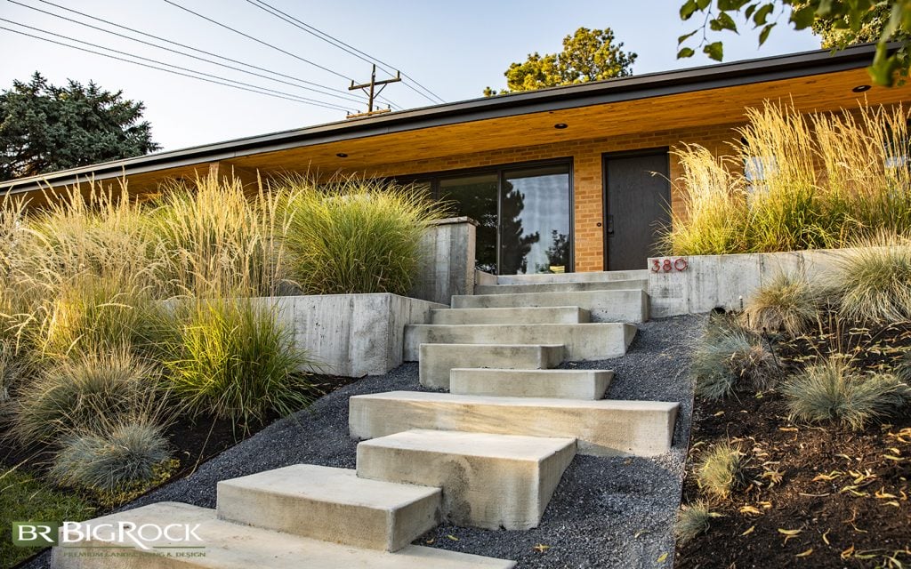 Xeriscape with modern cement stairs offset with grass gardens and cement rock wall garden beds.