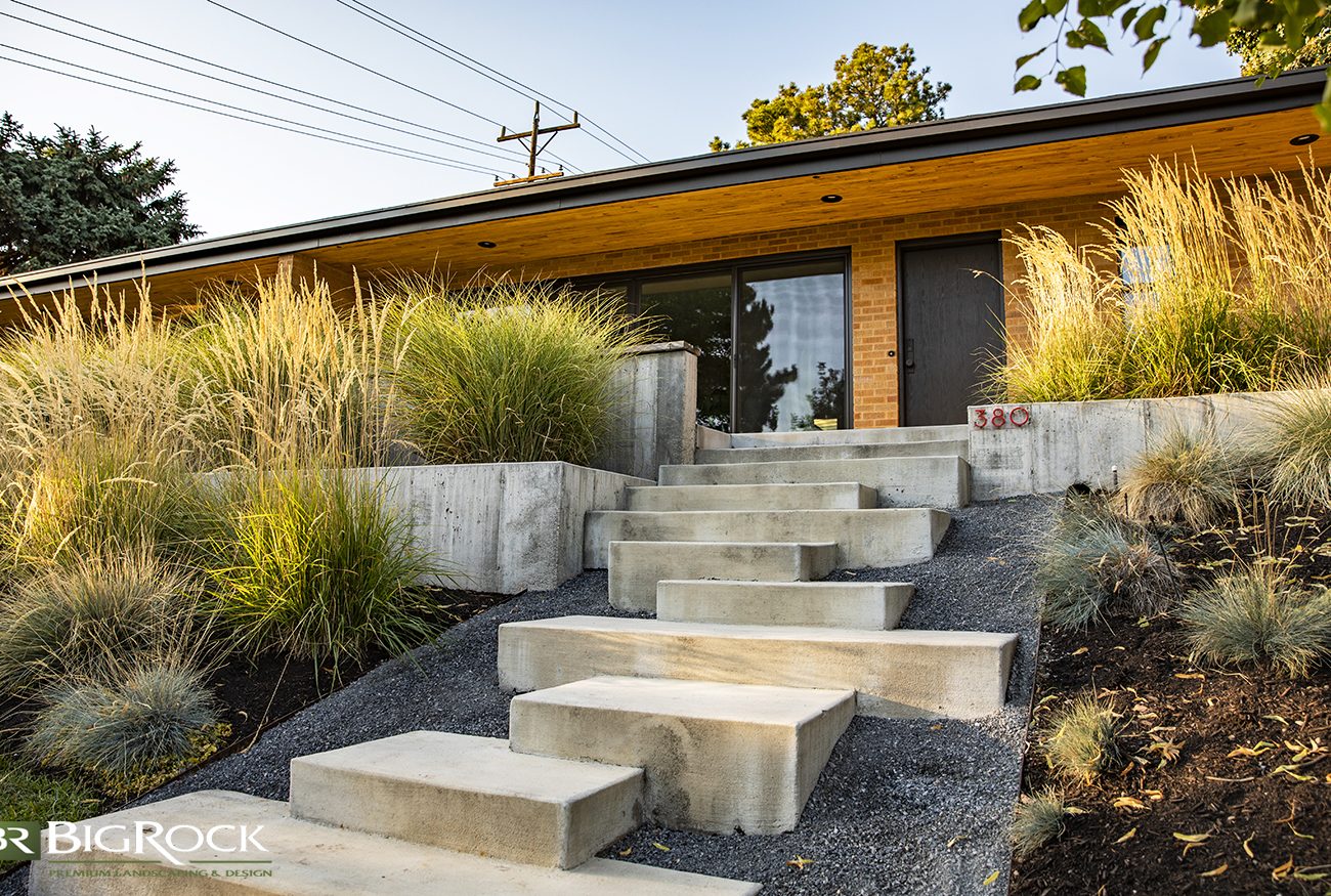 Xeriscape with modern cement stairs offset with grass gardens and cement rock wall garden beds.