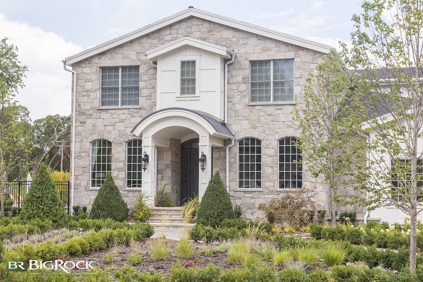 Beautiful two story stone home with a symmetrical xeriscape front yard landscaping with bark and no lawn for easy maintenance.