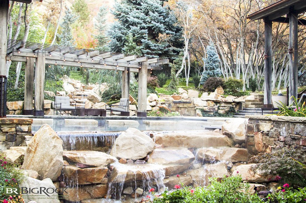 The rock water feature, the tall trees, the aged timber pergola, and the carefully placed greenery are all mountainside perfection.