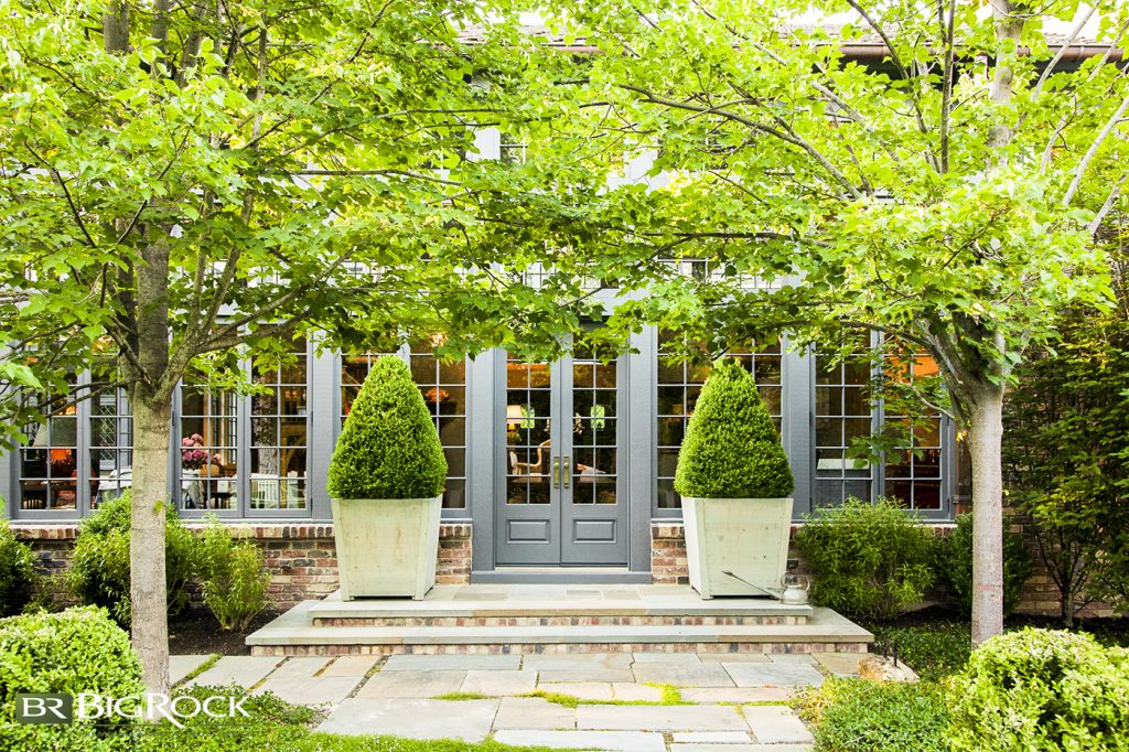 With leafy overhangs, tidy shrubs in stone containers, and natural materials like concrete and brick, this landscape design is dripping with old-world charm