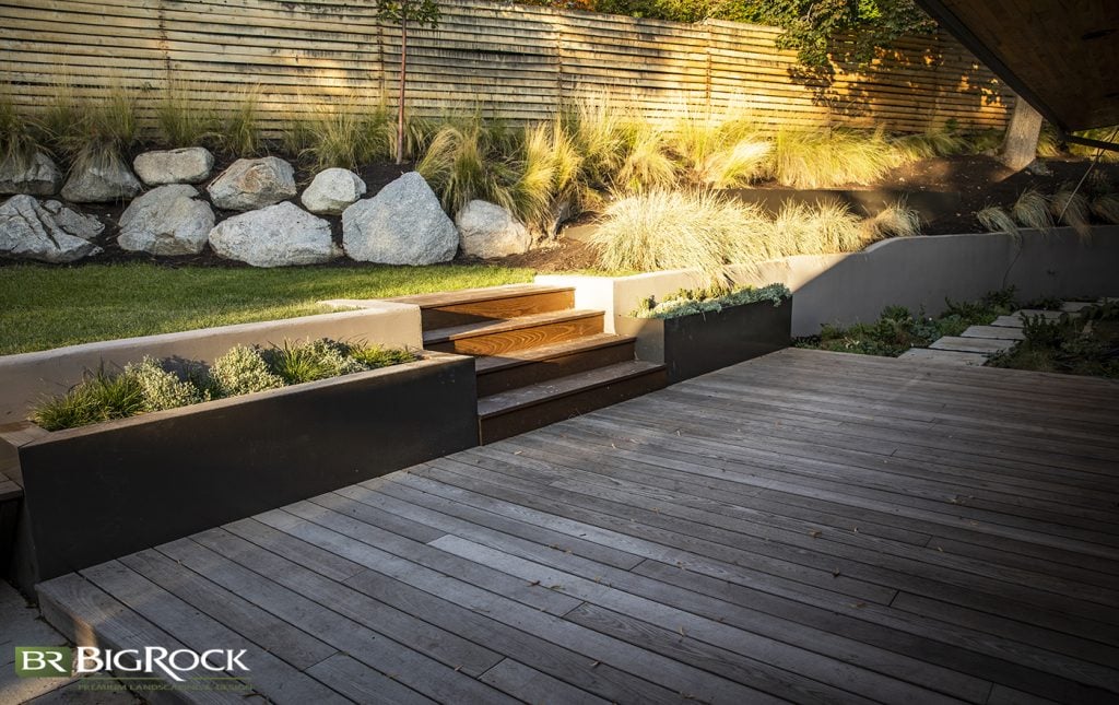 This homeowner used natural materials like concrete and stone to create borders and planters. They also used wood on the decking and stairs to bring warmth and contrast to the design.