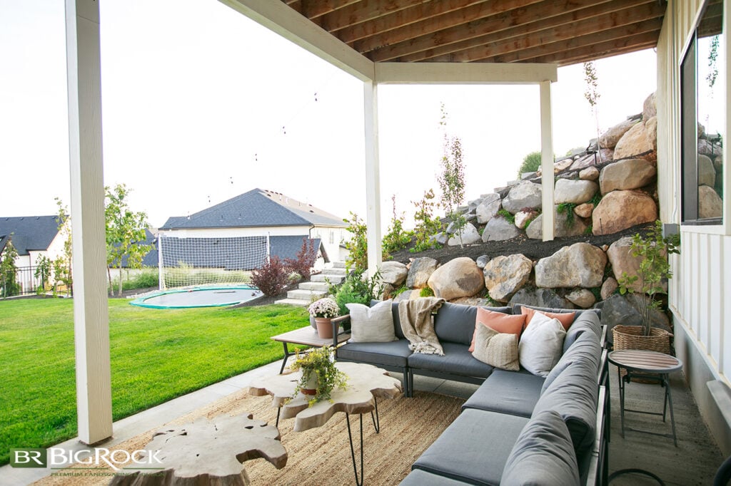 If you live in a hilly neighborhood, you might have a walk-out basement to your backyard. Don’t let a retaining wall make your backyard an eyesore; use it to add interest! This backyard living space feels cozy, private, and inviting because of the boulder retaining wall and the plants within it